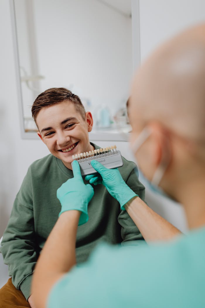 Smiling teen having teeth shade matched by dentist in an office.